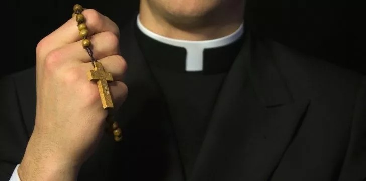 Un preot care ține un colier cu o cruce